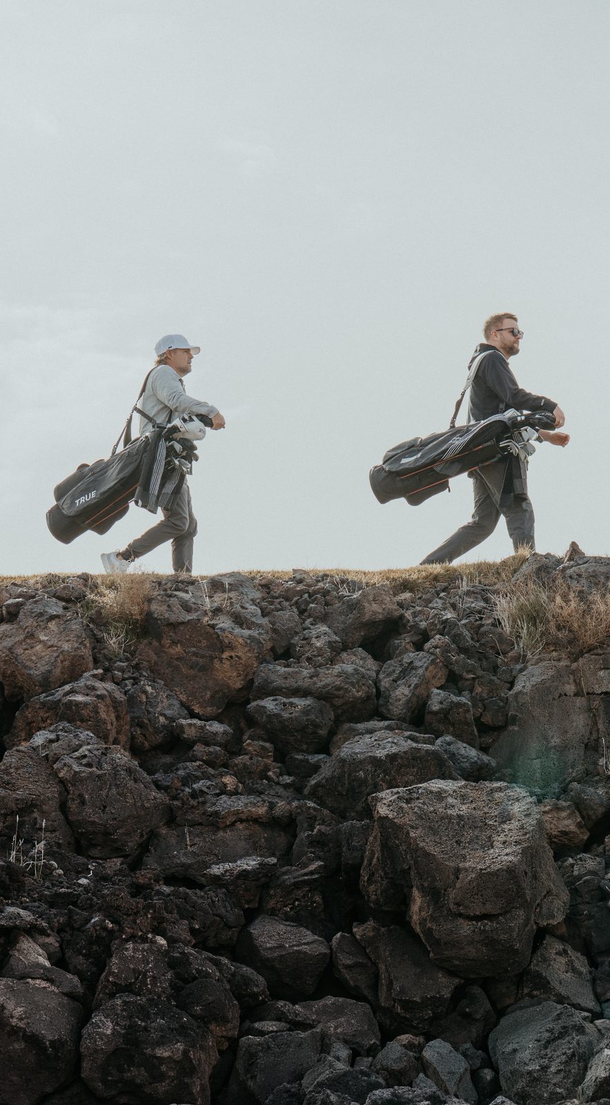 Two golfers carrying their bags along a ridge